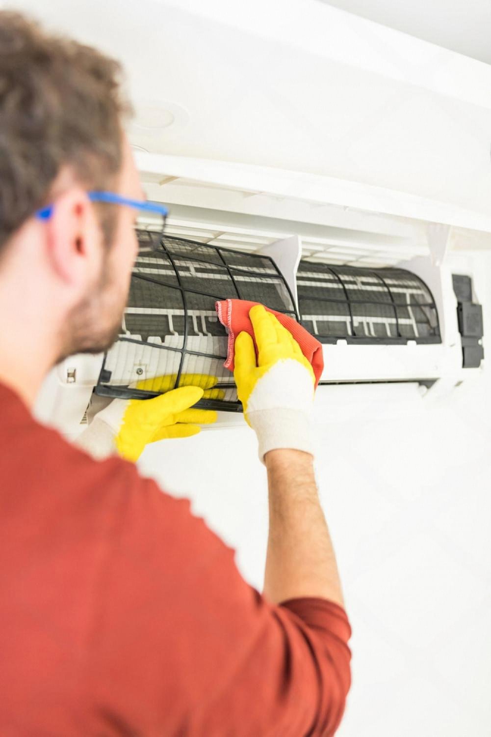 Man in gloves wiping dust from an air conditioner filter during routine maintenance